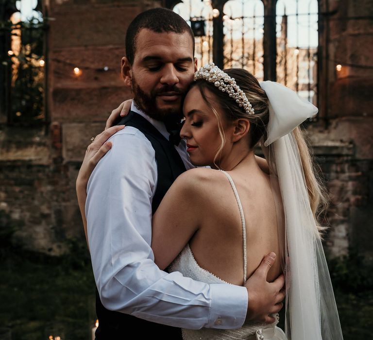 Bearded groom embracing his bride wearing a pearl headband and bow wedding veil 