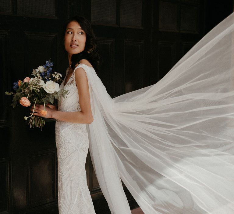 Bride wearing an Eliza Jane Howell wedding gown with embroidered bead and sequin details, and a flowing cape veil