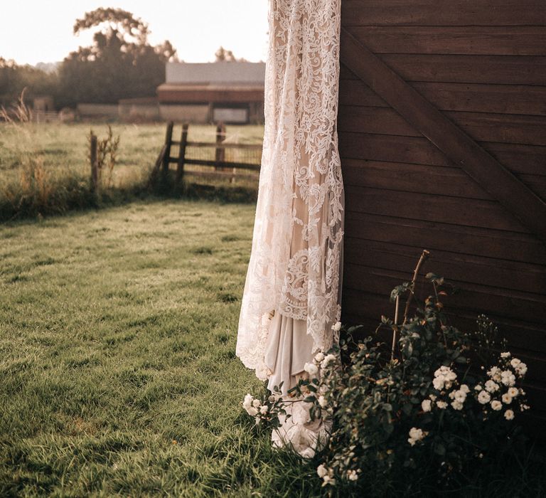 A lace boho wedding dress hangs from a wooden structure. 