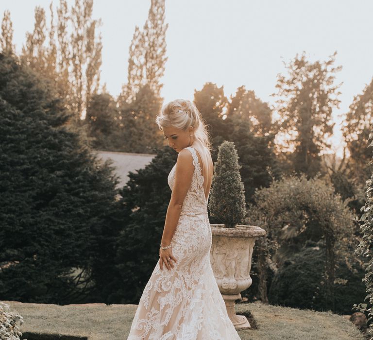 A bride in a long lace wedding dress stands in gardens for Crab & Lobster fairytale wedding.