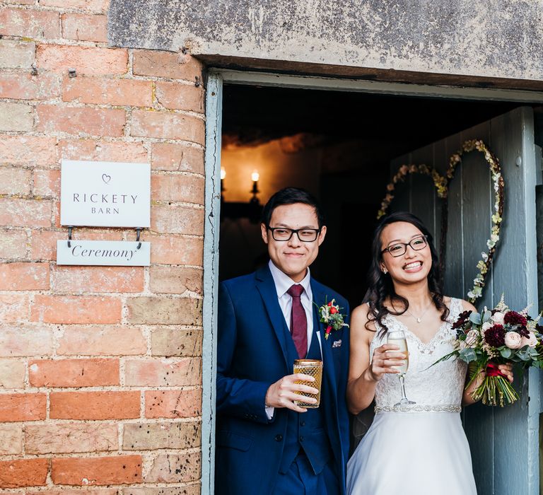 Bride & groom walk through doorway whilst holding wine glasses on their wedding day