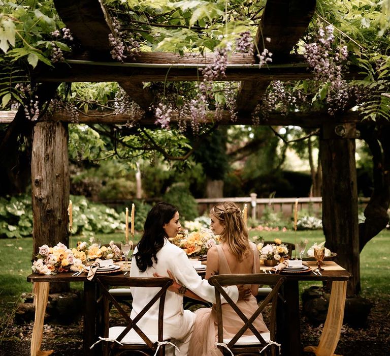 Two brides sitting at their outdoor wedding reception with honey yellow wedding decor 