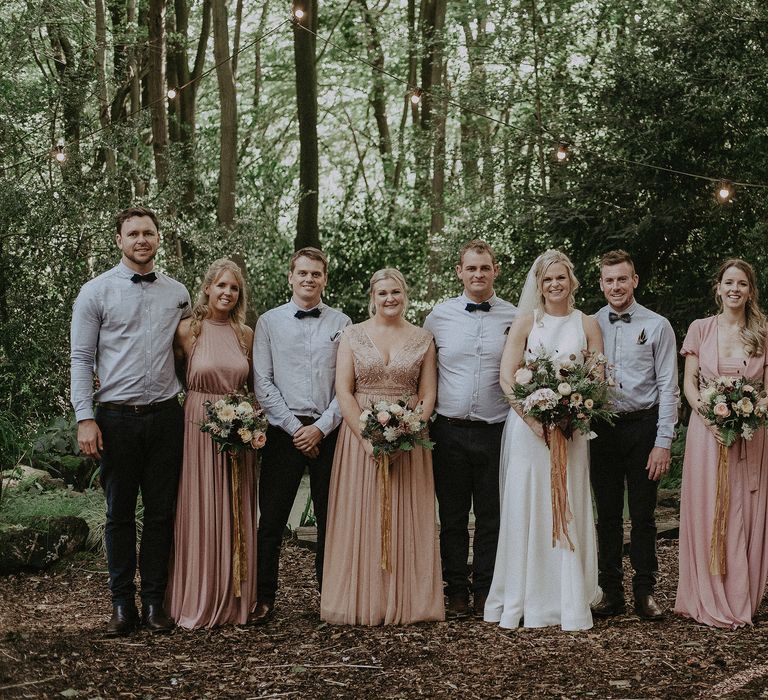 Bride & groom stand with their groomsmen and bridesmaids outdoors in the woodland on their wedding day