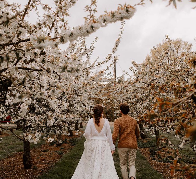 Bride and groom portrait amongst the trees with the bride in a low V back jumper and lasercut lace wedding skirt and groom in chino's trainers and a brown cable knit jumper 