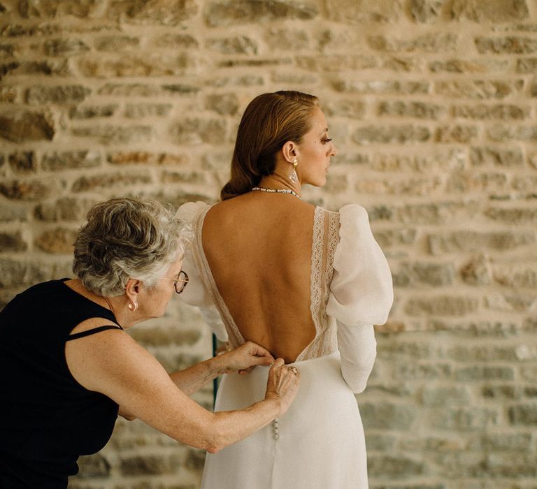 Wedding guest does up brides buttons to the back of her wedding gown