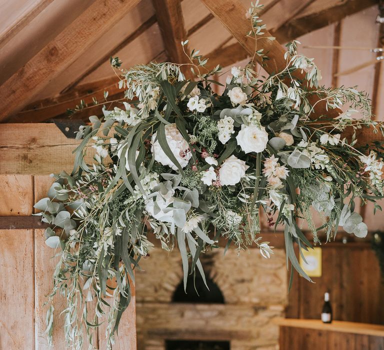 White, green and pink flower cloud hung from wooden beam at Tythe Barn wedding with barn wedding flowers