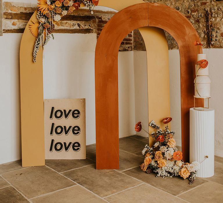 Contemporary wedding ceremony backdrop with geometric stands, contemporary signs and yellow and orange floral arrangements 