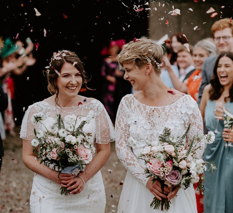 Confetti moment at Woolas Barn with two brides in a embellished gown and appliqué wedding dress holding matching pink and white wedding bouquets  