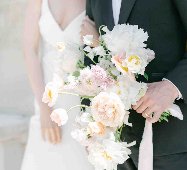 Groom holding a pastel flower wedding bouquet with roses, peonies, Icelandic poppies, sweet peas, scabious, foxglove, and snapdragons