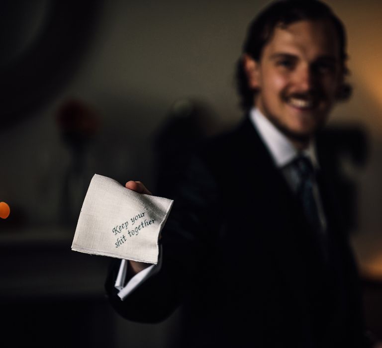 Groom in three piece suit holds handkerchief with 'Keep your shit together' embroidered in green thread for Cornish wedding 