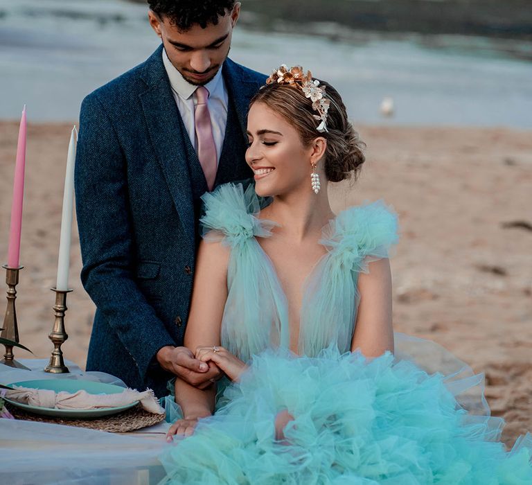 Beautiful bride with pinned updo and gold headband wearing a mint green wedding dress holding hands with there groom in a blue wool suit at their coastal beach elopement 