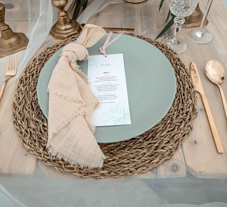 Place setting with wicker place mat, green plate and gold cutlery 