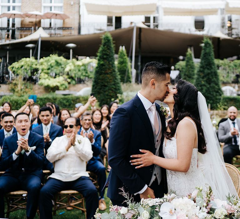 Wedding party clap with happiness as loved up couple kiss 