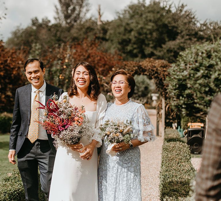 Bride becomes emotional as she walks down the aisle with her father and mother as the sun shines