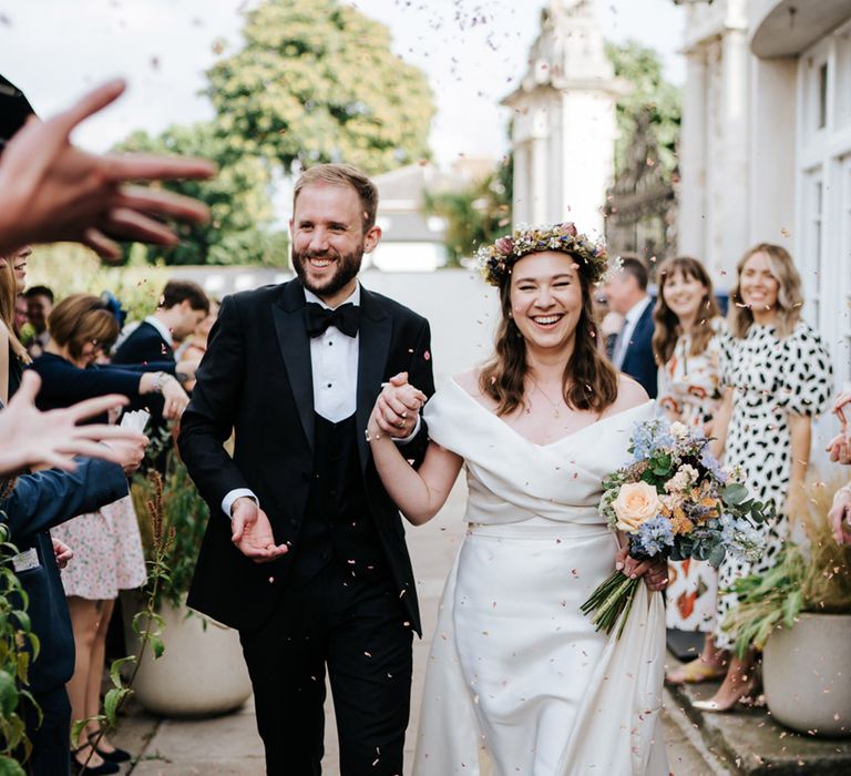 Bride & groom walk together after Hampton Court Wedding as bride holds pastel florals and wears flower crown