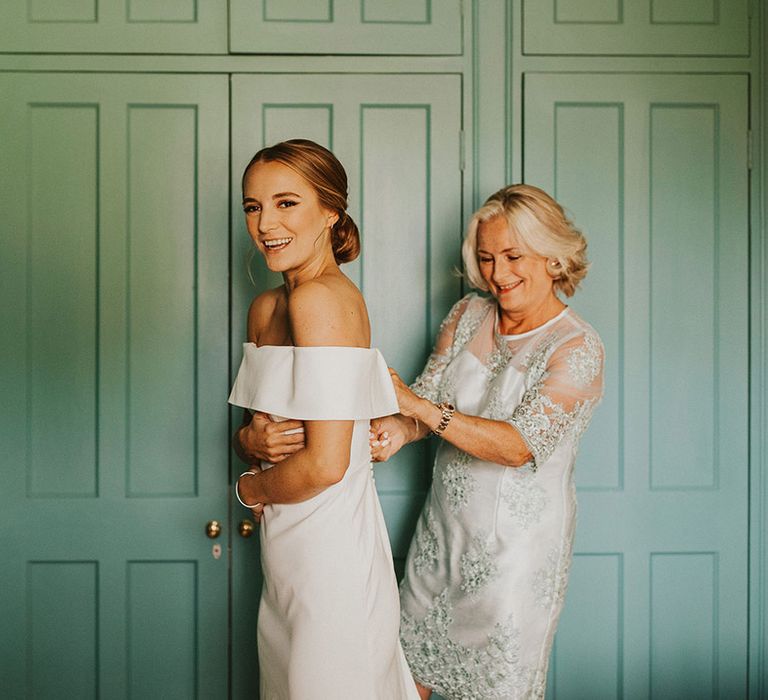 Mother of The Bride does up wedding gown for bride who wears off the shoulder wedding gown and hair pulled back into low bun