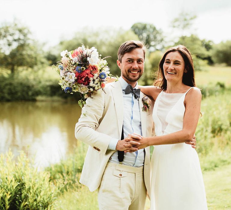 Bride & groom hold hands outdoors as bride holds colourful bouquet