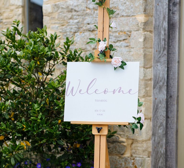 Wedding welcome sign on a wooden easel decorated with rose vine 