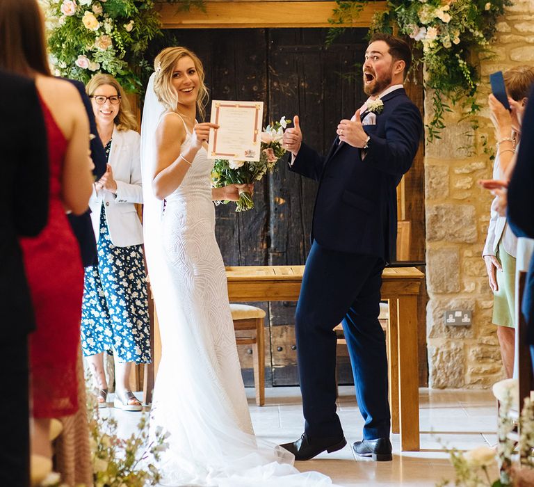 Bride in a fitted Made With Love bridal gown holding up the marriage certificate at their Caswell House wedding ceremony 