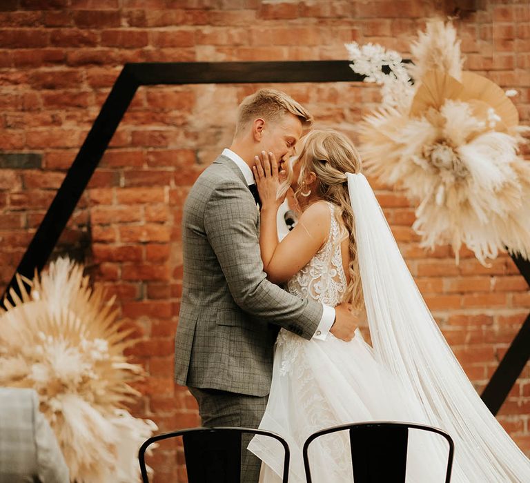 Bride and groom kiss at civil ceremony with geometric backdrop and pampas grass decor