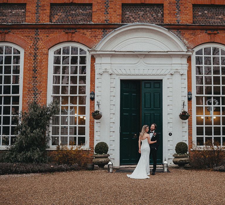 Bride & groom stand in front of green door on their wedding day at Gosfield Hall 