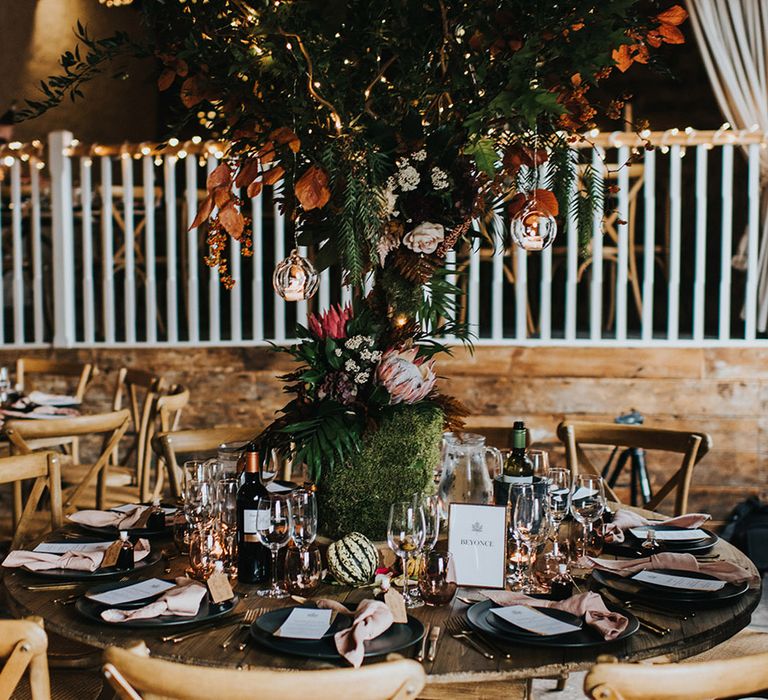 Round tables at autumn theme wedding with tree centrepieces, pumpkins and string lights decor 