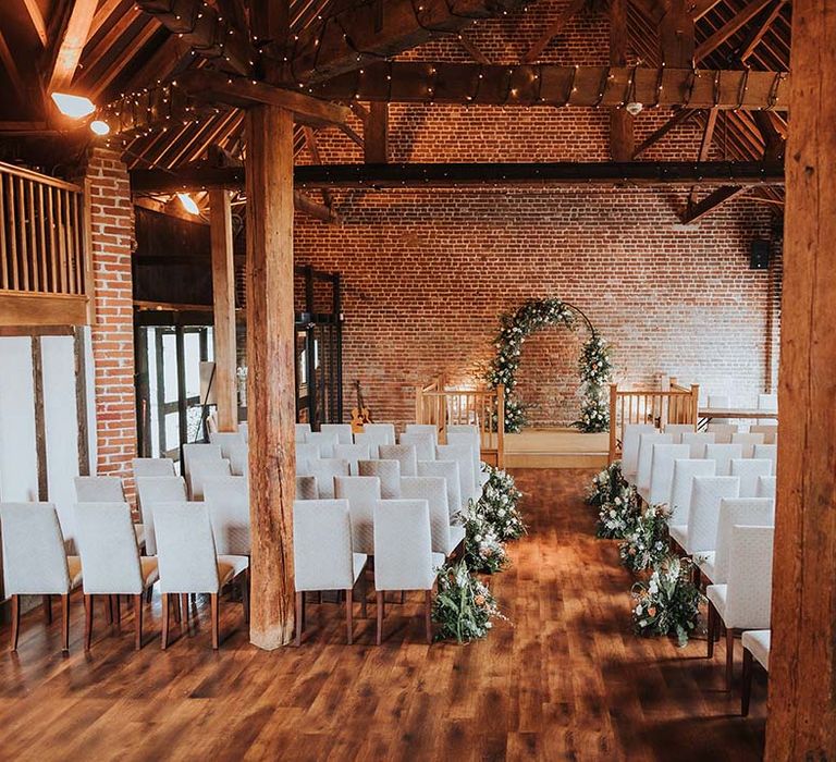 Rustic barn wedding venue in Kent with white tall back chairs and fairy lights