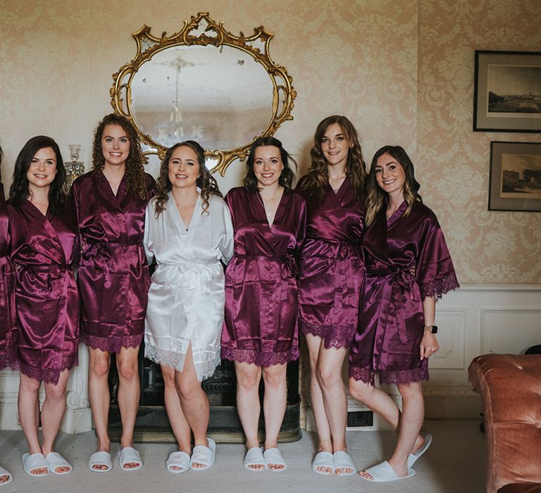 Bride in white satin robe with lace cuff details and slippers with bridesmaids wearing matching slippers with purple robes