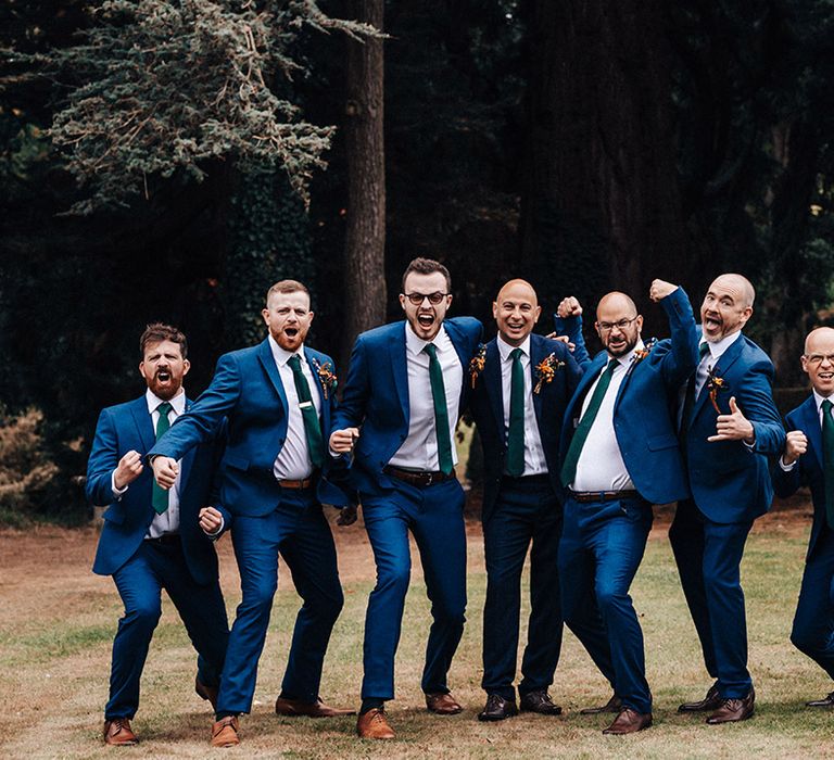 Groom in darker blue suit and tie with groomsmen in brighter blue suits and green ties with autumnal orange and red buttonholes