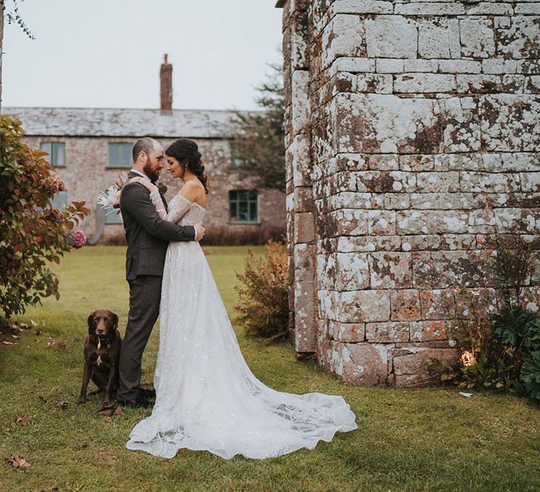 Bride and groom hug together and rest their foreheads together as their pet dog poses next to them