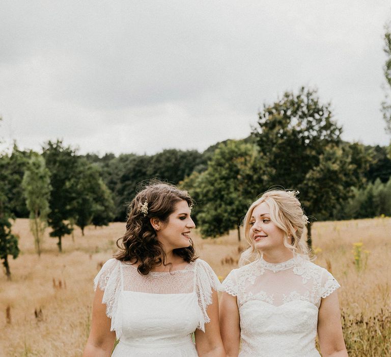 Brides glance at each other and hold hands as they walk with colourful bouquets