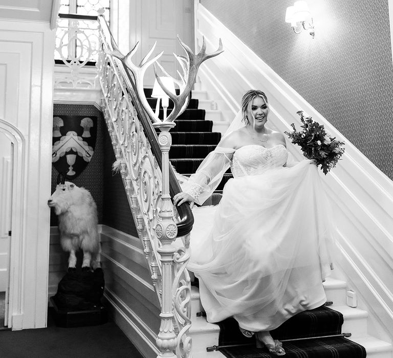 Bride in strapless wedding dress with sheer sleeves descends the stairs at castle wedding venue