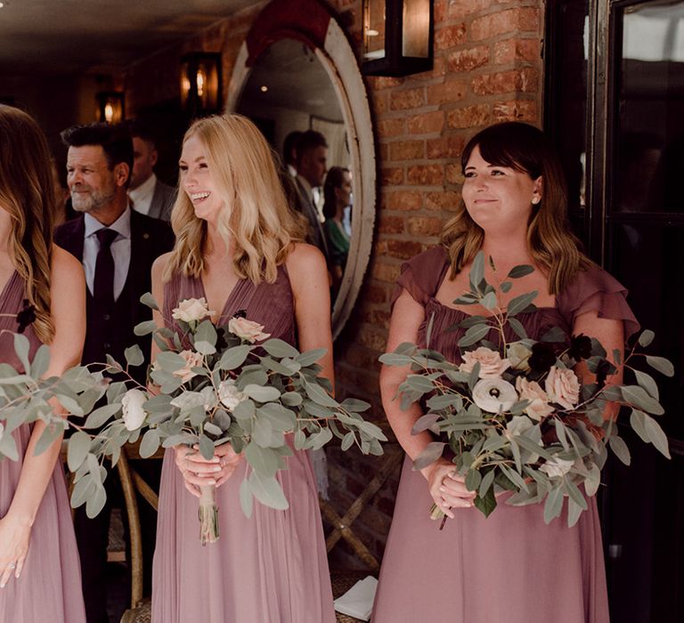 Bridesmaids in purple two tone dresses with pink rose bouquets with lots of green foliage