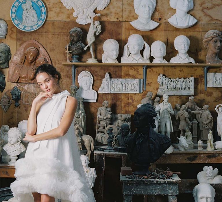 Bride in high low wedding dress with ruffles, train, and a bow and white wedding shoes with stiletto heel, ankle strap and white flower