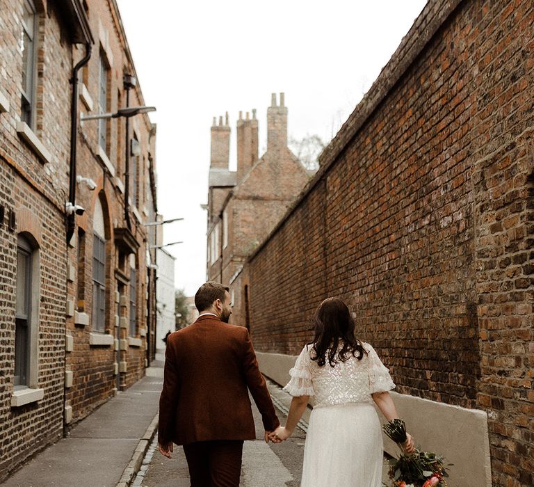 Bride in sparkly Needle and Thread top and skirt separates with block heel gold shoes walks the city with groom in a brown suit 