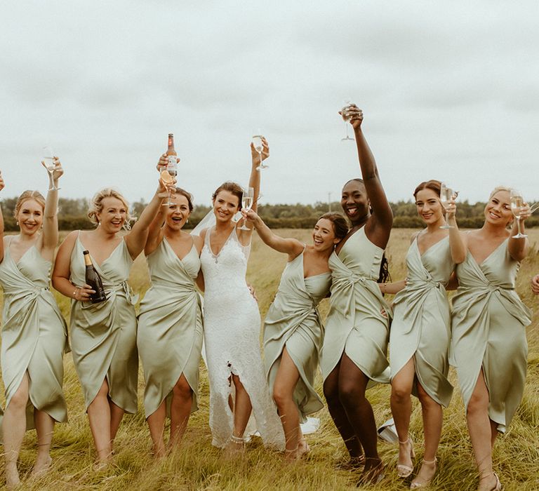 Bridesmaids make a toast in their sage green wrap dresses with bride in lace wedding dress 