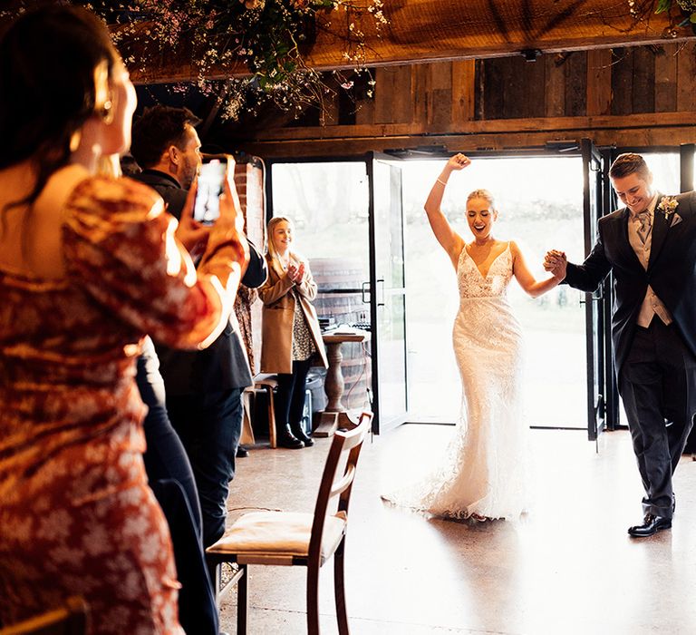 Wedding guests stand and clap as the bride and groom dance into their wedding reception