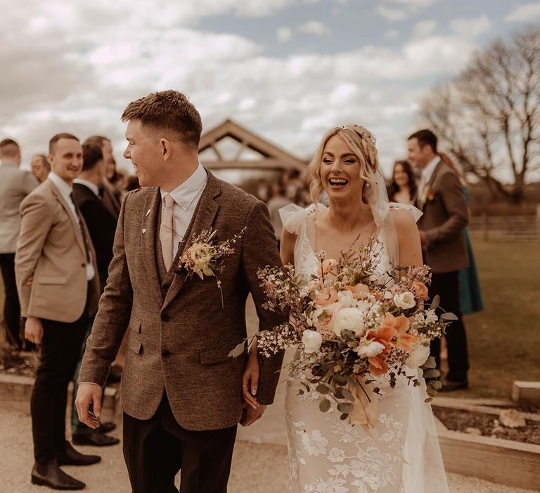 Bride in lace wedding dress with groom in brown three piece suit have confetti exit from barn wedding ceremony 