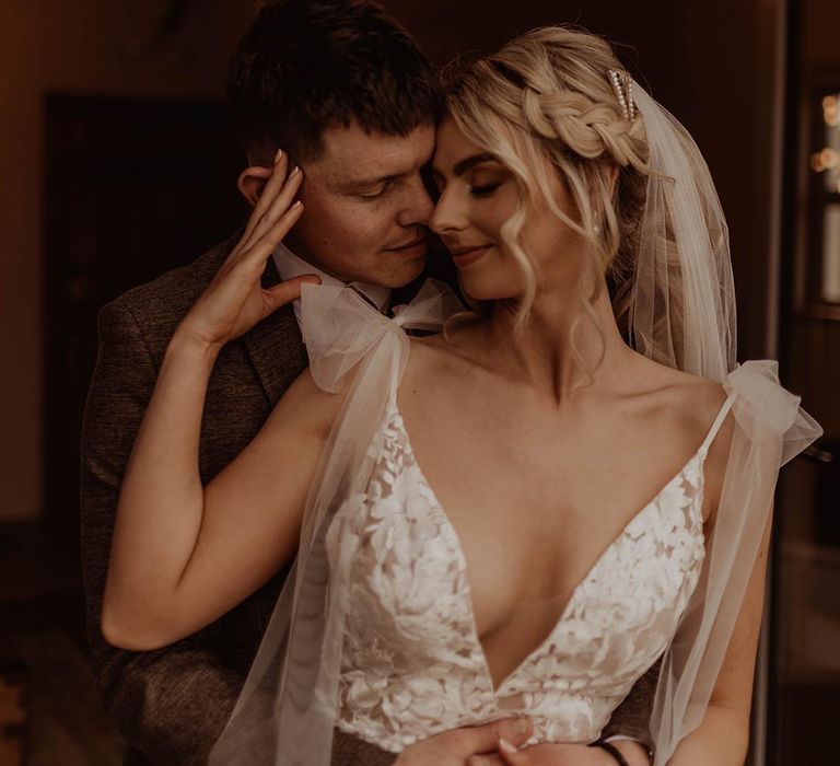 Bride in v-neck lace wedding dress with bow sleeves and pearl earrings and diamanté hair clip with groom for rustic barn wedding 