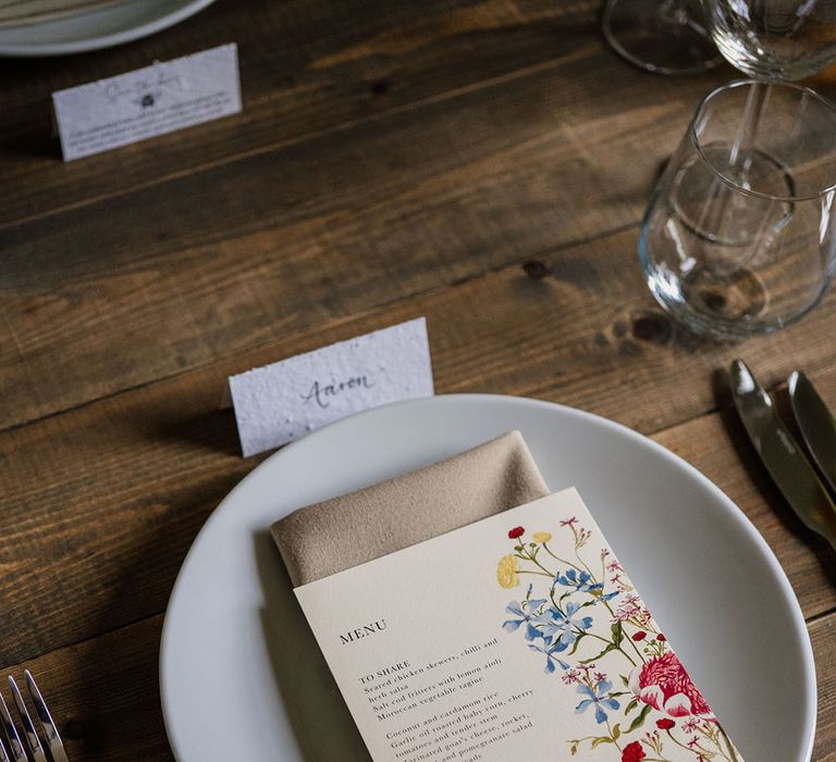 White plate and beige napkin with white menu card decorated with bright flower design 