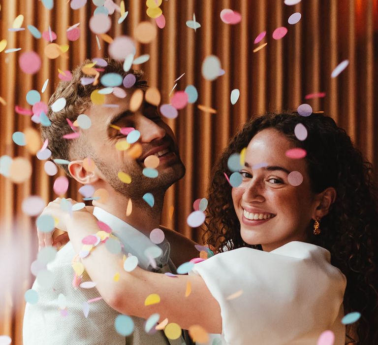 Colourful confetti moment with groom in a pale green suit and bride in a short wedding dress 