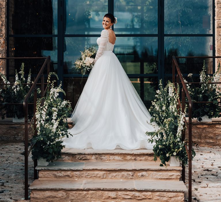 Bride holding large white and green wedding bouquet in Emma Beaumont wedding dress with tulle princess skirt and ruffle detail with hair bow 