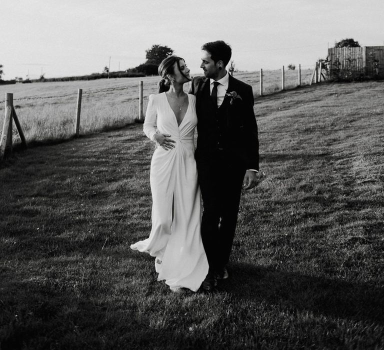 Bride in long sleeve wedding dress walking with groom around the grounds of The Barn at Botley Hill wedding venue 