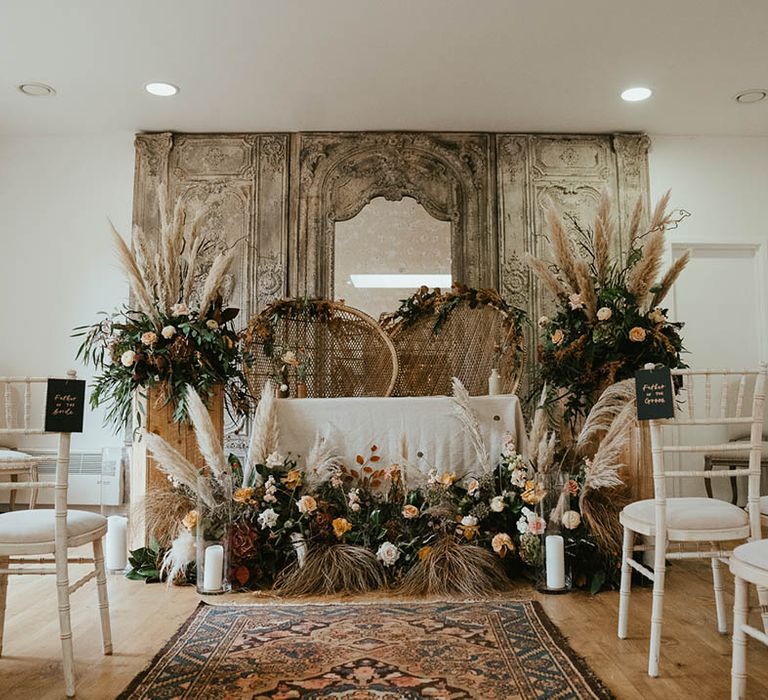 Altar decorations with pampas grass, peacock chairs and pillar candles in hurricane vases 