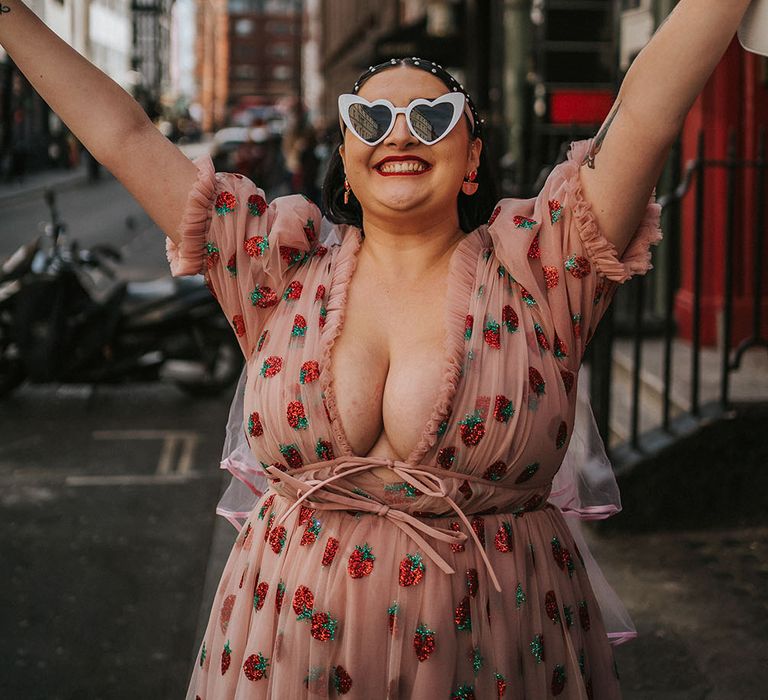 Bride wears heart-shaped sunglasses and pink chiffon dress with plunge neckline and glitter strawberries 