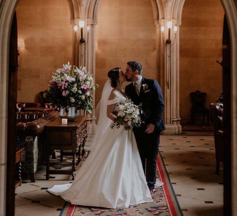 Groom in a blue suit kisses bride in an off the shoulder dresses 