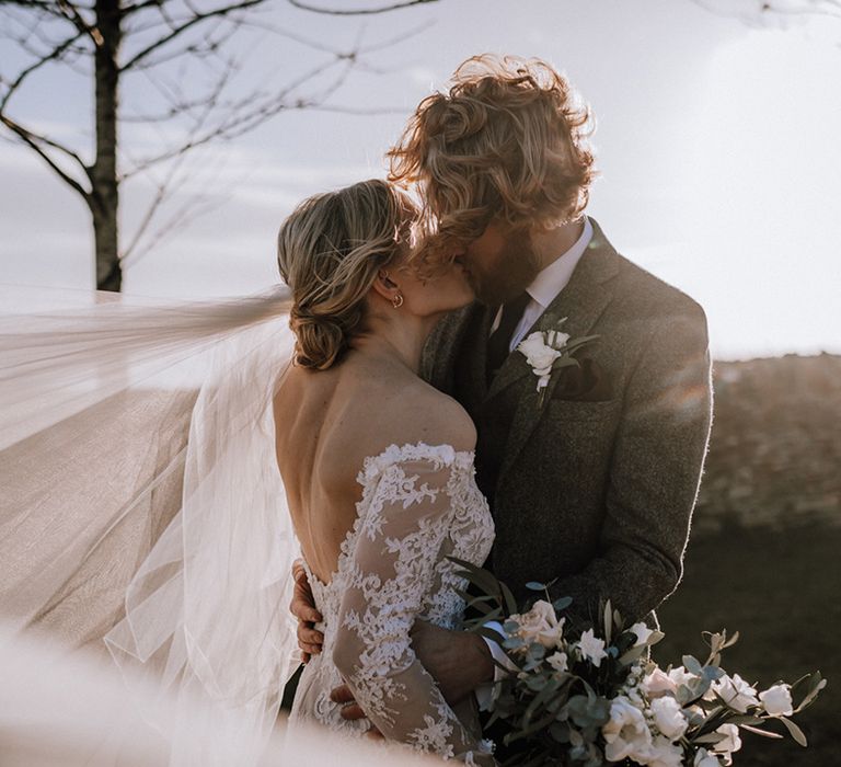 Bride and groom kiss during golden hour at their rustic wedding 