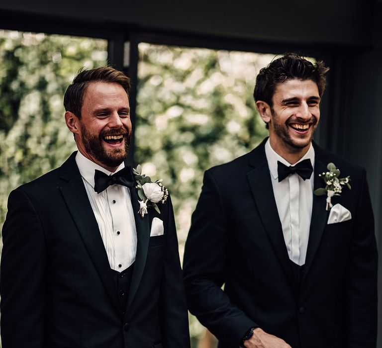 Groom and the best man stand in their black tie as they get the first look at the bride 