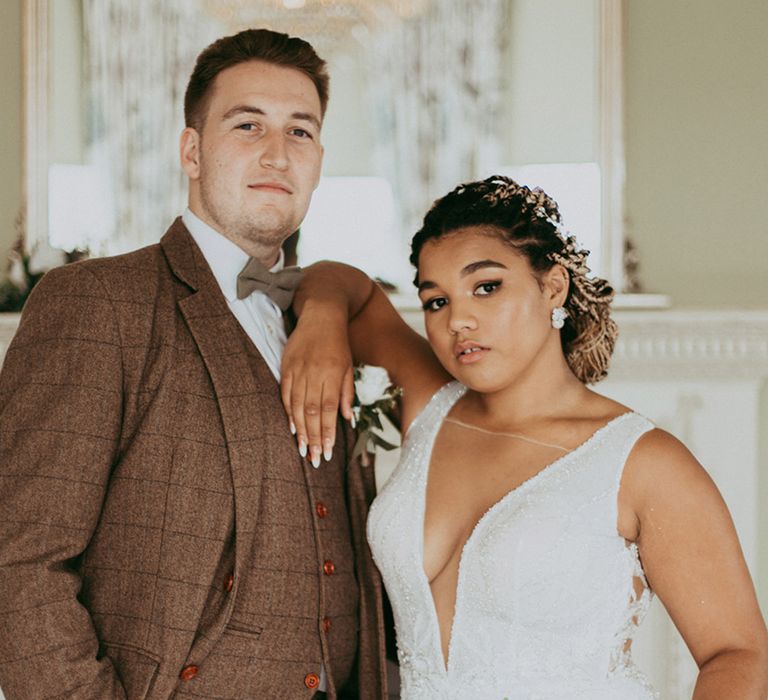 Groom in a brown checkered three piece wedding suit with bride in a sparkly plunging wedding dress with white flower bouquet 