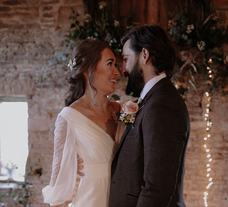 Bride in a long sleeve sequin wedding dress with her hair in a messy braid and silver hair accessories with the groom in a brown suit and pink rose buttonhole 